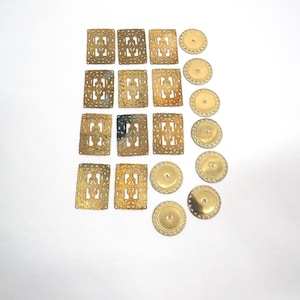 May include: A collection of gold-toned metal findings consisting of eleven rectangular pieces with an intricate openwork filigree pattern and seven circular pieces featuring a smooth center and a decorative scalloped edge border.