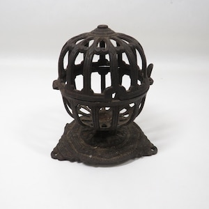 May include: A dark brown, antique-style metal sphere with an openwork design, resembling a cage. The sphere sits on a decorative base with a floral pattern. The object appears to be a decorative item or container.