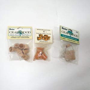 May include: Three packages of miniature craft wood items. One package contains small wooden flower pots, another contains miniature clay pots, and the third contains a small wooden water bucket. The packages are labeled "Craftwood".