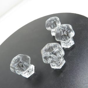May include: A set of four clear glass knobs, each featuring a hexagonal shape with a faceted surface and a central circular opening. The knobs are arranged in a cluster, showcasing their transparent material and geometric design from a top-down view.