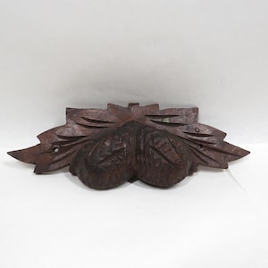 May include: A dark brown wooden carved ornament featuring two acorns surrounded by leaves.