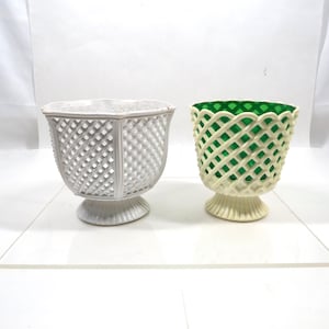 May include: Two decorative ceramic planters. One is white with a lattice design, the other is off-white with a green interior and lattice design. Both planters have a pedestal base.