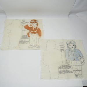 May include: Two vintage fabric panels with hand-drawn illustrations of dolls. One depicts a paratrooper in an orange jumpsuit and goggles, saluting. The other shows a girl in a blue jacket and skirt, with a hat and purse. Both have text.