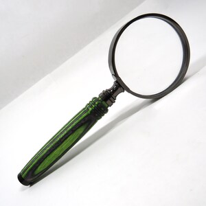 May include: A magnifying glass featuring a circular lens encased in a dark metallic frame. The handle is crafted from layered wood with a distinct pattern of alternating black and bright lime green stripes, ending in a solid black cap.