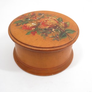 May include: A round, wooden box with a floral design on the lid. The box is a warm brown color, and the lid features a bouquet of roses in shades of red, orange, and yellow, with green leaves.