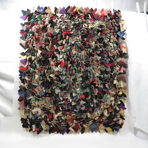 May include: A colorful rag rug made from scraps of fabric. The rug is rectangular and has a fringed edge. The rug is made up of a variety of colors, including red, green, blue, yellow, and brown.