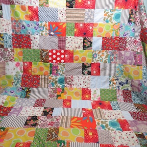 May include: A patchwork quilt made of colorful fabric squares. The quilt is made of a variety of fabrics, including floral prints, geometric patterns, and solid colors. The quilt is a vibrant and cheerful piece of home decor.