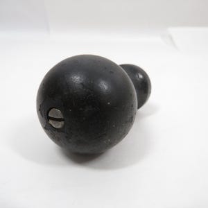 May include: A black, round wooden knob with a smaller, attached knob. The knob has a screw head visible on the side. The object is set against a white background.