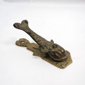 May include: A vintage brass nutcracker in the shape of a fish. The fish has detailed scales and fins, with a hinged mouth for cracking nuts. The base is rectangular with a decorative edge. The nutcracker is a unique kitchen tool.