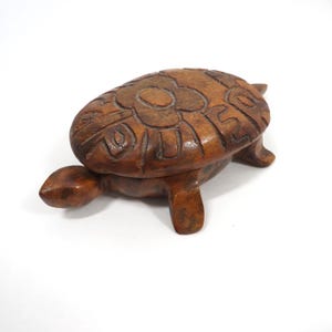 May include: A carved wooden turtle ornament with a detailed design on its shell. The turtle is brown and has a smooth, polished finish. The figurine is a decorative item, likely for display or as a collectible.