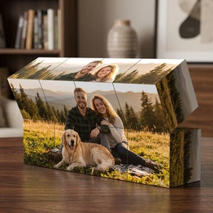 May include: A rectangular photo block puzzle composed of twelve individual cubes arranged in a grid. The surface displays a continuous outdoor photograph of a couple sitting in a grassy field with a golden retriever, set against a mountain backdrop.