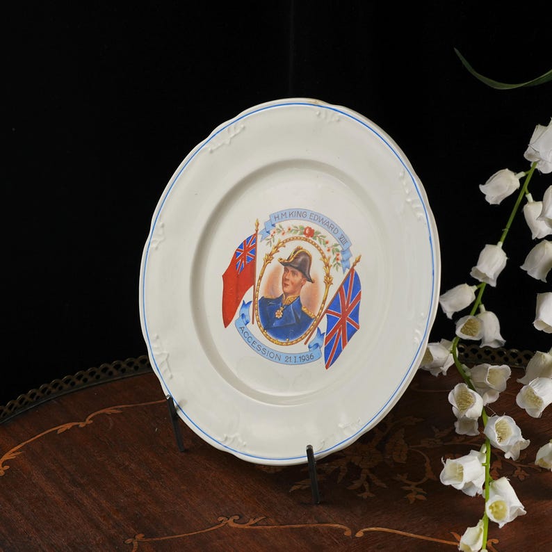 K&ouml;nnte beinhalten: Ein wei&szlig;er Keramikteller mit einem zentralen Portr&auml;t von K&ouml;nig Edward VIII. in Milit&auml;runiform, flankiert von einer roten Flagge und dem Union Jack, mit dem aufgedruckten Text H.M. KING EDWARD VIII und ACCESSION 21.I.1936 auf der Oberfl&auml;che.