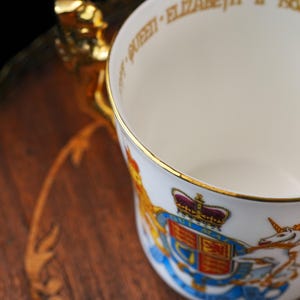 Puede incluir: Una taza de porcelana blanca con borde dorado y asa dorada. El exterior muestra un colorido escudo de armas real con una corona, un le&oacute;n y un unicornio. El borde interior tiene la inscripci&oacute;n QUEEN ELIZABETH II.
