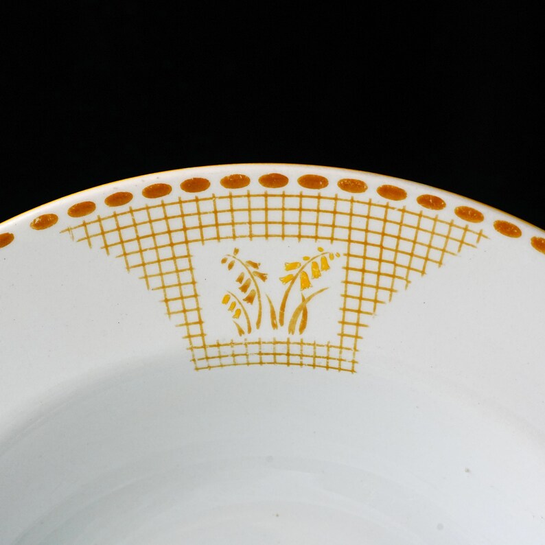 May include: White ceramic plate with a gold floral design and a gold grid pattern. The plate has a gold dotted border. The floral design is in the center of the plate.