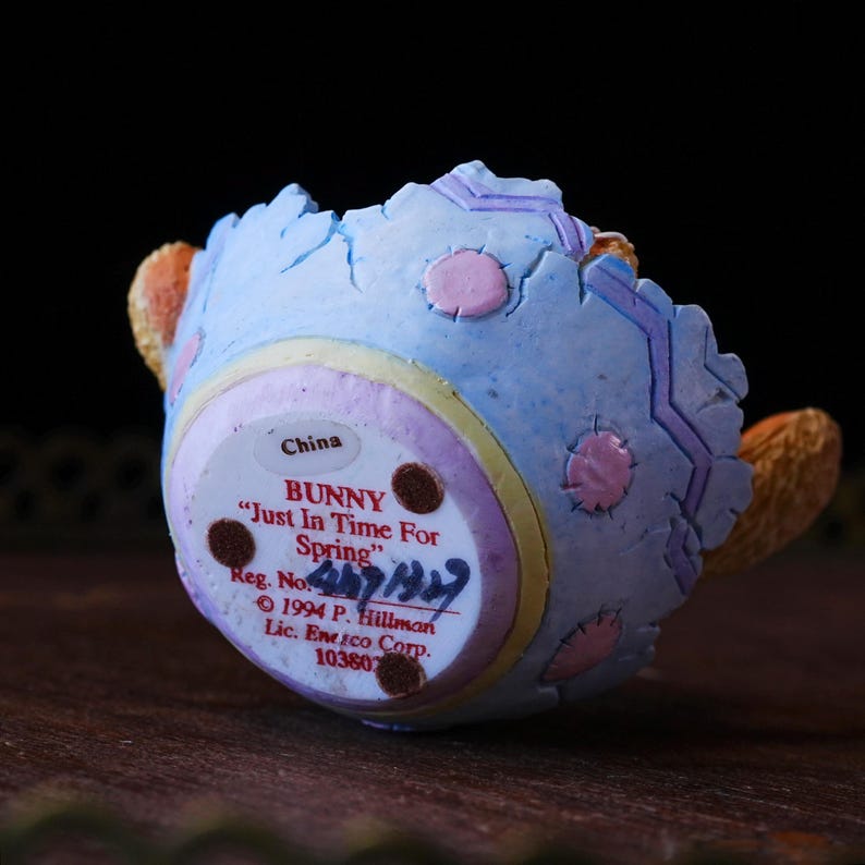 May include: A ceramic bunny figurine, viewed from the bottom, with a light blue eggshell design and pink accents. The text "BUNNY Just In Time For Spring" is visible, along with the registration number and copyright information.