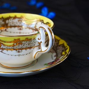 Peut inclure: Un ensemble tasse et soucoupe en porcelaine blanche avec un bord jaune vif, des d&eacute;tails en filigrane dor&eacute; et un motif g&eacute;om&eacute;trique en losanges. La tasse poss&egrave;de une anse incurv&eacute;e avec un liser&eacute; dor&eacute; et la soucoupe pr&eacute;sente un motif floral.
