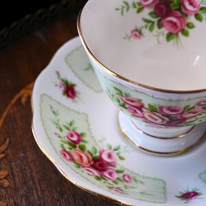 K&ouml;nnte beinhalten: Wei&szlig;es Tee-Service mit Rosenmuster. Die Tasse und Untertasse haben einen Goldrand und einen hellgr&uuml;nen Hintergrund. Die Rosen sind rosa und rot. Ideal f&uuml;r Teepartys.
