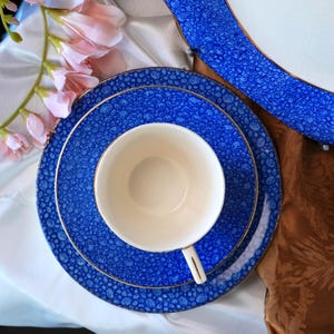 May include: A blue and white patterned tea set with gold trim. The set includes a teacup, a saucer, and a dinner plate. The teacup is white, and the plates are blue with a white pattern. The set is arranged on a white surface.