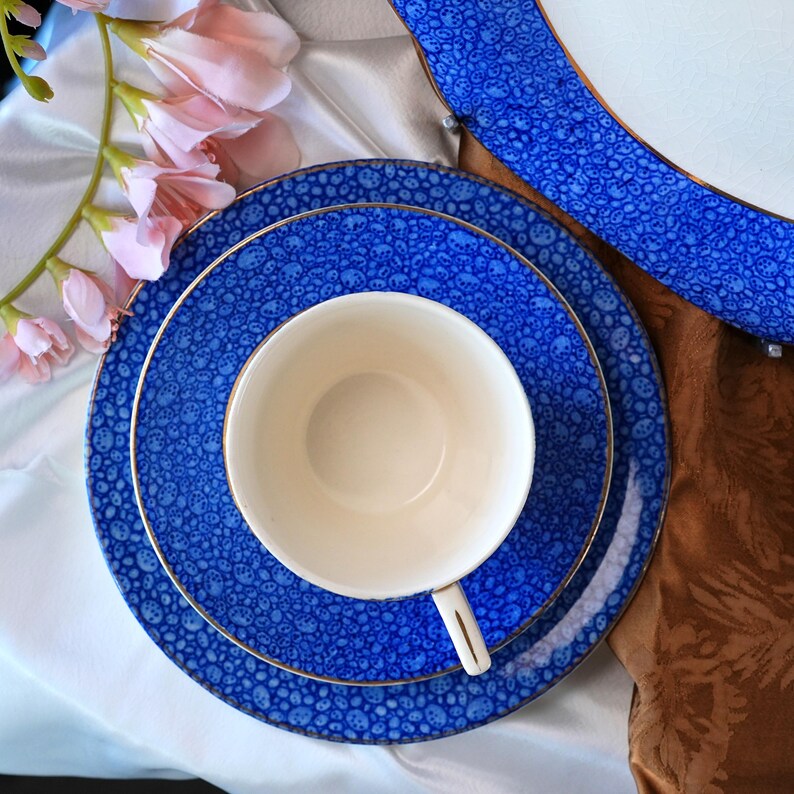 May include: A blue and white patterned tea set with gold trim. The set includes a teacup, a saucer, and a dinner plate. The teacup is white, and the plates are blue with a white pattern. The set is arranged on a white surface.