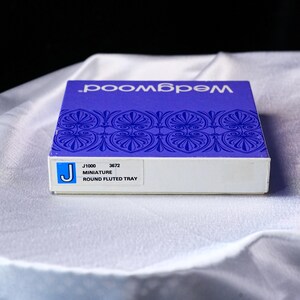 May include: A rectangular product box with a blue top featuring the white text Wedgwood and a repeating blue floral pattern. A white label on the side displays the text J1000 3672 MINIATURE ROUND FLUTED TRAY with a blue square containing a white letter J.