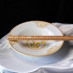 May include: White ceramic bowl with a gold rim and floral design. The bowl has a diameter of approximately 10 inches. The bowl's design includes a gold grid pattern and yellow floral accents.