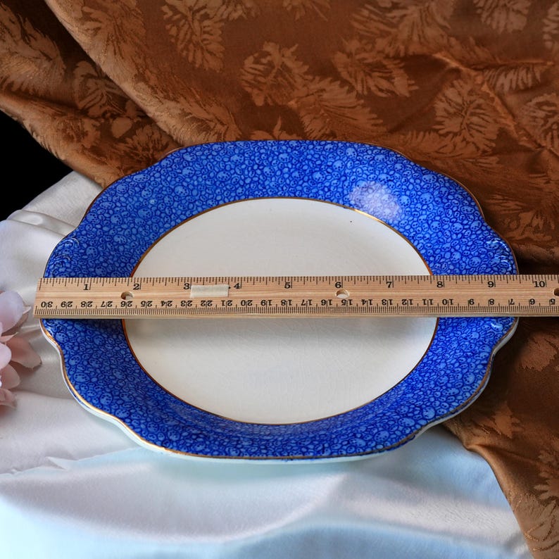May include: An oval serving platter with a white center and a blue patterned border. The rim has a scalloped edge and a gold trim. The platter measures approximately 12 inches in length.