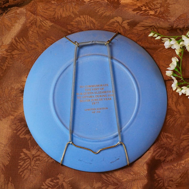 May include: A blue commemorative plate with a wire plate hanger. The plate has text that reads "To commemorate the visit of Queen Elizabeth Ottawa during the Silver Jubilee Year 1977". Limited edition.