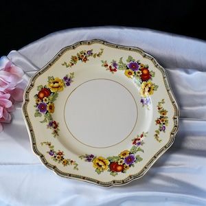 Puede incluir: Un plato octogonal crema con un dise&ntilde;o floral. El plato presenta flores amarillas, moradas y rojas con hojas verdes. Un borde dorado y un borde negro y verde completan el dise&ntilde;o. Probablemente vintage.