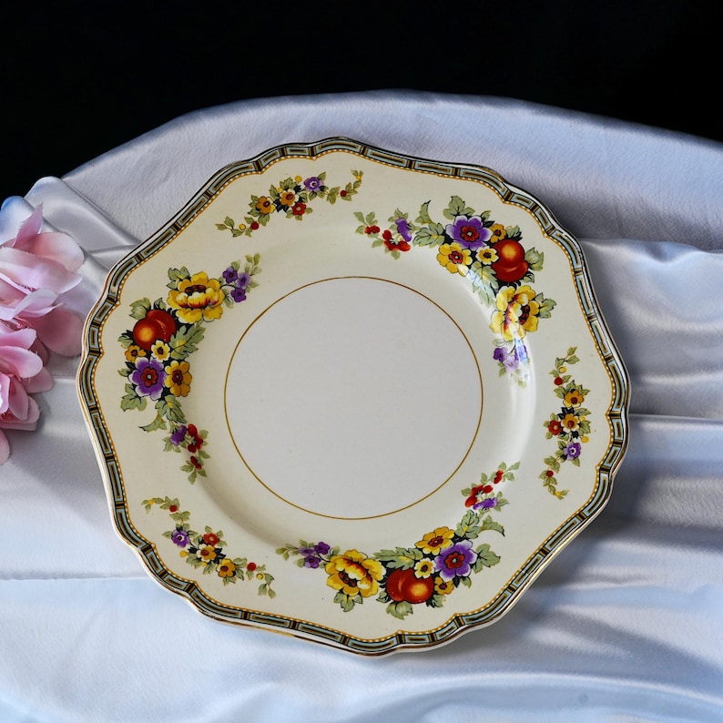 Puede incluir: Un plato octogonal crema con un dise&ntilde;o floral. El plato presenta flores amarillas, moradas y rojas con hojas verdes. Un borde dorado y un borde negro y verde completan el dise&ntilde;o. Probablemente vintage.