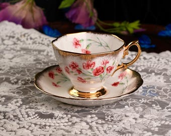 May include: A vintage teacup and saucer set. The white porcelain cup and saucer are adorned with red floral patterns and gold trim. The cup has a gold handle and sits on a matching saucer, creating an elegant tea set.