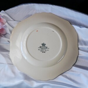 Puede incluir: Plato de cer&aacute;mica blanquecina con borde festoneado. La parte inferior presenta un emblema central y texto, incluyendo "John Maddock & Sons Ltd England". El plato tiene una forma irregular y un aspecto vintage.