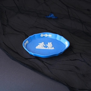 May include: An oval blue ceramic tray featuring white relief figures of two people interacting in the centre, with white floral and leaf-like decorative accents along the scalloped rim, showcasing a classic matte finish and raised detailing.