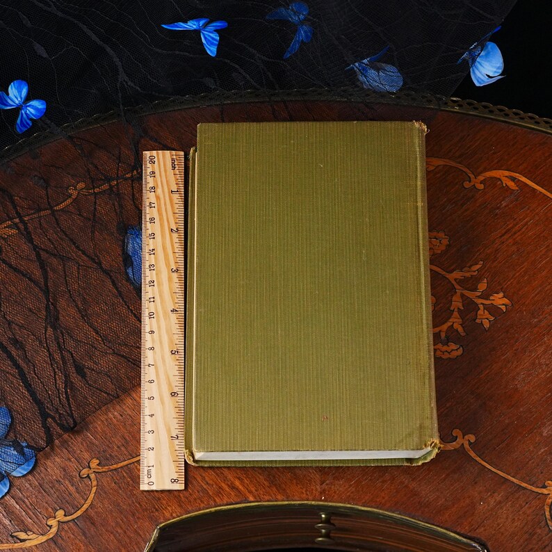 Puede incluir: Un libro de tapa dura rectangular con una cubierta de tela verde oliva texturizada. Una regla de madera est&aacute; colocada verticalmente a lo largo del lado izquierdo del libro, mostrando una longitud de unos 20 cm para la cubierta.