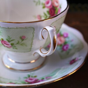 K&ouml;nnte beinhalten: Ein Vintage-Tee-Set aus wei&szlig;em Porzellan. Die Tasse und Untertasse sind mit einem zarten Blumenmuster aus rosa Rosen und gr&uuml;nen Bl&auml;ttern verziert. Goldene Verzierungen s&auml;umen die R&auml;nder und den Henkel und verleihen dem Set Eleganz.