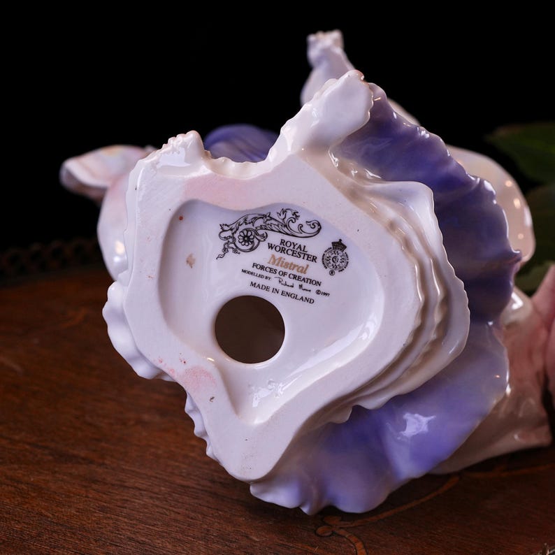 May include: A Royal Worcester Mistral porcelain figurine with a white and lilac floral design. The base of the figure is visible, displaying the Royal Worcester mark and "Made in England" text.