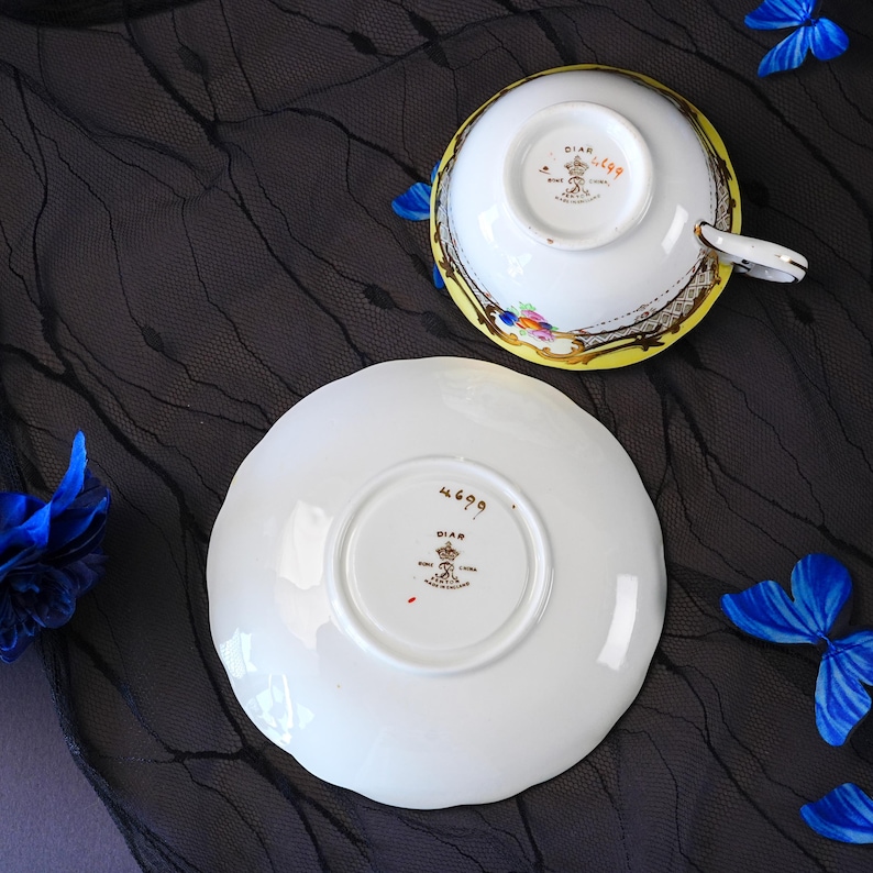 Peut inclure: Un ensemble tasse et soucoupe en porcelaine blanche avec un bord jaune, des d&eacute;tails dor&eacute;s et des motifs floraux. Le dessous des deux pi&egrave;ces porte la marque Diar Bone China, Made in England, ainsi que le num&eacute;ro 4699 peint &agrave; la main.