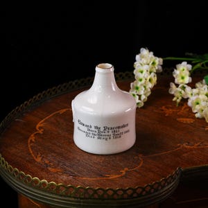 K&ouml;nnte beinhalten: Eine wei&szlig;e Keramikflasche mit rundem K&ouml;rper und schmalem Hals. Die Flasche tr&auml;gt schwarzen Text mit der Aufschrift "Edward the Peacemaker" und Details zu seinem Leben. Die Flasche steht auf einem Holztisch mit floralen Akzenten.
