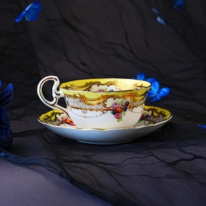 Peut inclure: Un ensemble tasse et soucoupe en porcelaine avec un bord jaune vif orn&eacute; de d&eacute;tails en filigrane dor&eacute;. La surface en c&eacute;ramique blanche est d&eacute;cor&eacute;e d'un petit bouquet color&eacute; de fleurs et de fruits peints, incluant des roses et des baies.