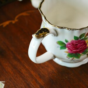 Peut inclure: Un pot &agrave; lait en porcelaine blanche avec un bord festonn&eacute; dor&eacute;, une anse incurv&eacute;e orn&eacute;e de d&eacute;tails dor&eacute;s et un motif floral de roses roses avec des feuilles vertes. Le pot pr&eacute;sente un corps cannel&eacute; et une finition lisse et brillante.