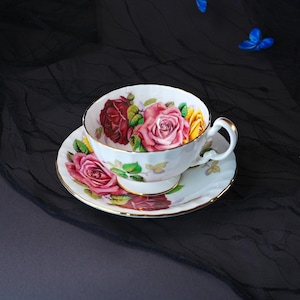 Peut inclure: Une tasse &agrave; th&eacute; et sa soucoupe en porcelaine blanche orn&eacute;es d'un motif floral compos&eacute; de roses rouges, roses et jaunes avec des feuilles vertes. Le bord de la tasse et de la soucoupe est soulign&eacute; par un fin liser&eacute; dor&eacute;, avec une anse courb&eacute;e.