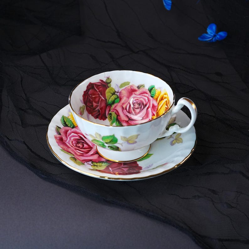 Peut inclure: Une tasse &agrave; th&eacute; et sa soucoupe en porcelaine blanche orn&eacute;es d'un motif floral compos&eacute; de roses rouges, roses et jaunes avec des feuilles vertes. Le bord de la tasse et de la soucoupe est soulign&eacute; par un fin liser&eacute; dor&eacute;, avec une anse courb&eacute;e.