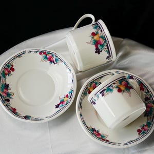 Może przedstawiać: Biały porcelanowy zestaw do herbaty z motywem owoc&oacute;w i kwiat&oacute;w. Zestaw zawiera dwie filiżanki do herbaty z uchwytami i dwa spodki. Krawędzie filiżanek i spodk&oacute;w zdobi obramowanie z owoc&oacute;w i liści.