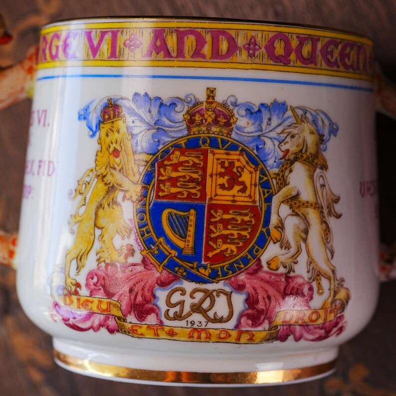 Puede incluir: Taza de cer&aacute;mica blanca con borde y asa dorados, con un escudo real con un le&oacute;n y un unicornio, y el texto "GEORGE VI AND QUEEN". La taza tambi&eacute;n tiene el a&ntilde;o 1937.