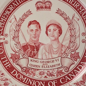 May include: A commemorative ceramic plate featuring a red and white transfer print of King George VI and Queen Elizabeth. The design includes a crown, flags, maple leaves, and the text: COMMEMORATION TO THE DOMINION OF CANADA, KING GEORGE VI AND QUEEN ELIZABETH.