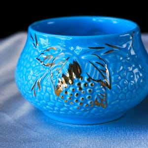 Op de afbeelding: Een felblauwe kom met een getextureerd, korrelig oppervlak en een goudkleurig metallic ontwerp met bladeren en bessen. De kom heeft een brede, ronde vorm met een gladde binnenkant en een consistente, levendige blauwe afwerking aan de buitenkant.