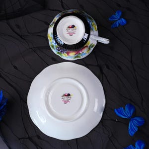 Op de afbeelding: Een Royal Albert bone china theekop en schotel set uit de Country Fare serie, patroon Kent. Het witte porselein is voorzien van een kleurrijk fruitmotief met druiven en appels. De onderkant van beide stukken toont het merk en de tekst.