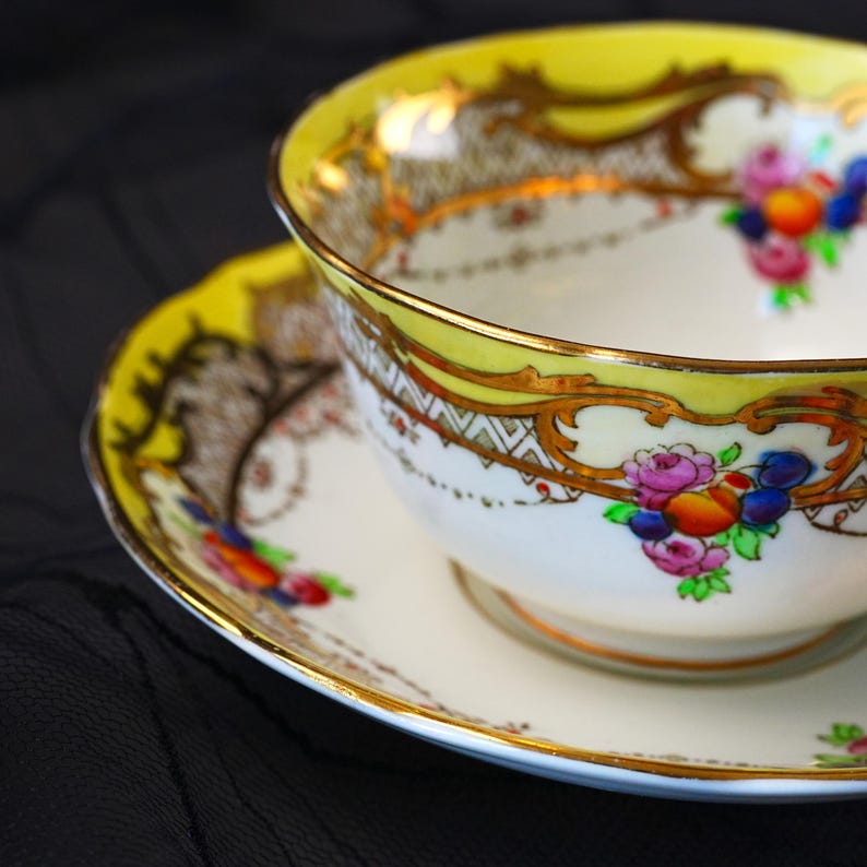 Peut inclure: Un ensemble tasse et soucoupe en porcelaine avec un bord jaune vif, des d&eacute;tails en filigrane dor&eacute; complexes et des motifs floraux peints &agrave; la main dans des tons de rose, bleu et orange. La base en c&eacute;ramique blanche est orn&eacute;e de dorures.