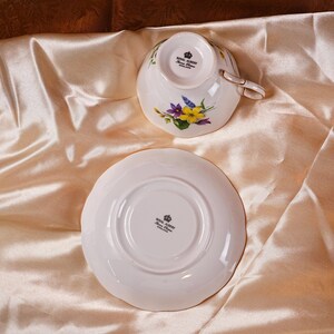 K&ouml;nnte beinhalten: Ein wei&szlig;es Royal Albert Tee-Set mit Tasse und Untertasse. Die Tasse und Untertasse haben ein Blumenmuster mit lila und gelben Bl&uuml;ten. Die Tasse hat einen goldenen Henkel. Das Royal Albert Logo ist sichtbar.