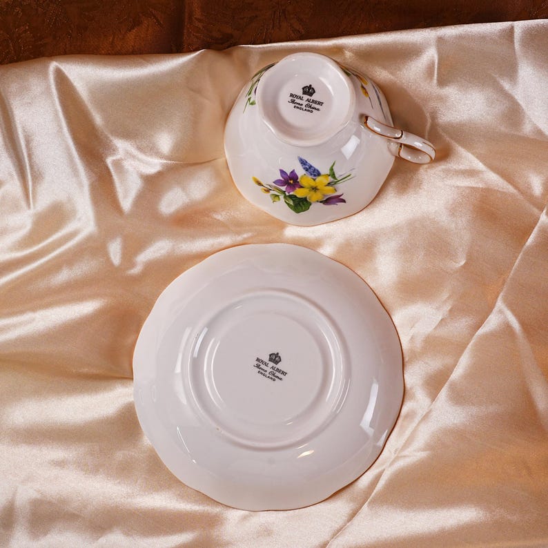 K&ouml;nnte beinhalten: Ein wei&szlig;es Royal Albert Tee-Set mit Tasse und Untertasse. Die Tasse und Untertasse haben ein Blumenmuster mit lila und gelben Bl&uuml;ten. Die Tasse hat einen goldenen Henkel. Das Royal Albert Logo ist sichtbar.