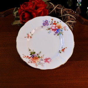 Puede incluir: Plato de porcelana blanca con borde festoneado y ribete dorado. El plato está decorado con un colorido estampado floral con flores rosas, moradas, azules y naranjas. Una pieza clásica para servir.